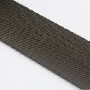 May include: A close-up of a dark green woven webbing strap with a herringbone pattern.