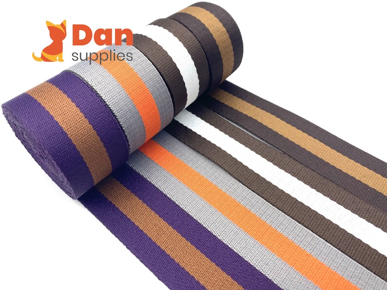 May include: A roll of striped webbing in five different colour combinations. The colours are purple, brown, orange, grey, and white. The webbing is 2 inches wide.