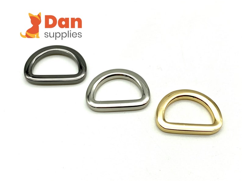 May include: Three D-rings in different finishes: silver, nickel, and gold. The D-rings are a common hardware finding used in crafting and jewelry making.