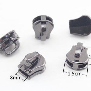 May include: Five black metal zipper pulls, each with a different design. The pulls are 1.5 cm wide and 1.7 cm tall. One pull is 8 mm wide.