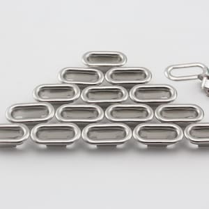 May include: A collection of silver-toned oval-shaped drawer pulls arranged on a white surface. The pulls are made of metal and have a recessed design. One pull is detached, showing the back and the loop.