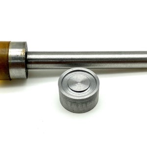 May include: A metal tool for setting eyelets, with a long handle and a round, silver-colored base. The tool has a yellow plastic piece on the top of the handle.