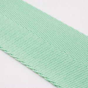 May include: A close-up of a light green woven ribbon with a herringbone pattern.
