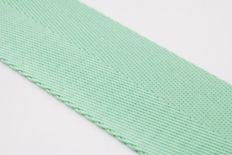 May include: A close-up of a light green woven ribbon with a herringbone pattern.