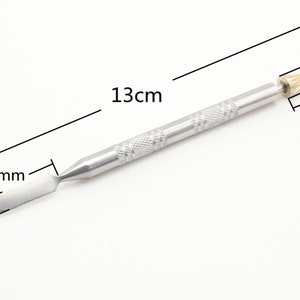 Op de afbeelding: Een zilveren metalen gereedschap met een puntige punt en een platte, afgeronde mes. Het gereedschap is 13 cm lang, het mes is 2,5 cm breed en de punt is 1,8 cm lang.