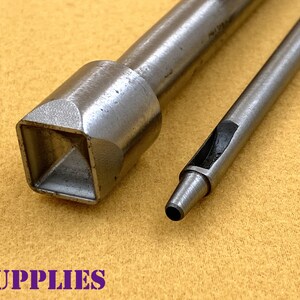 May include: Two metal leather hole punches. The larger punch has a square hole and the smaller punch has a round hole.