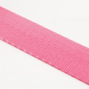 May include: Close-up of a vibrant pink woven ribbon. The ribbon has a textured surface with a diagonal pattern. The bright pink color is consistent across the ribbon.