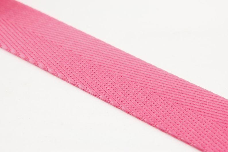 May include: Close-up of a vibrant pink woven ribbon. The ribbon has a textured surface with a diagonal pattern. The bright pink color is consistent across the ribbon.