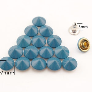 Può includere: Un gruppo di 15 borchie piramidali di colore blu-verde con base argentata e centro dorato. Le borchie sono disposte a forma di triangolo. L'immagine include le misure: 3 mm, 7 mm e 5 mm.