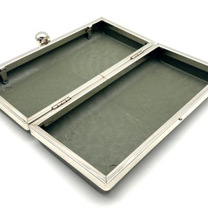 May include: An empty, open, gray, rectangular box with a silver metal frame and hinge. The box has a small silver knob on the top.