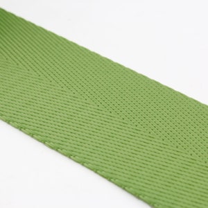 May include: A close-up of a green woven webbing strap. The strap has a herringbone pattern and is made of a durable material.