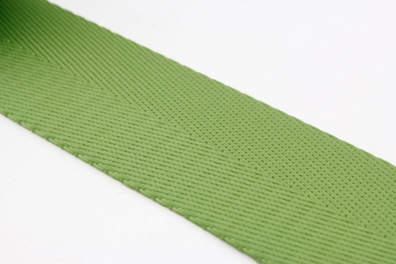 May include: A close-up of a green woven webbing strap. The strap has a herringbone pattern and is made of a durable material.