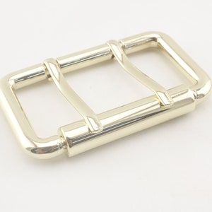 May include: A gold-toned metal buckle with a rectangular shape and a double-prong design.