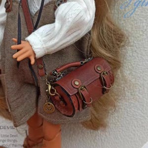 May include: A brown leather satchel with a metal chain strap and a brass buckle. The bag has a rolled top and a small metal tag with the number 32 on it.