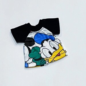 May include: A white t-shirt with a black and white image of Donald Duck and Mickey Mouse. The shirt has black sleeves and a black collar.