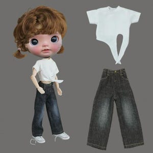 May include: A doll dressed in a white t-shirt and dark denim jeans, paired with white trainers. The doll has brown hair styled in pigtails. A spare white t-shirt and jeans are also shown.