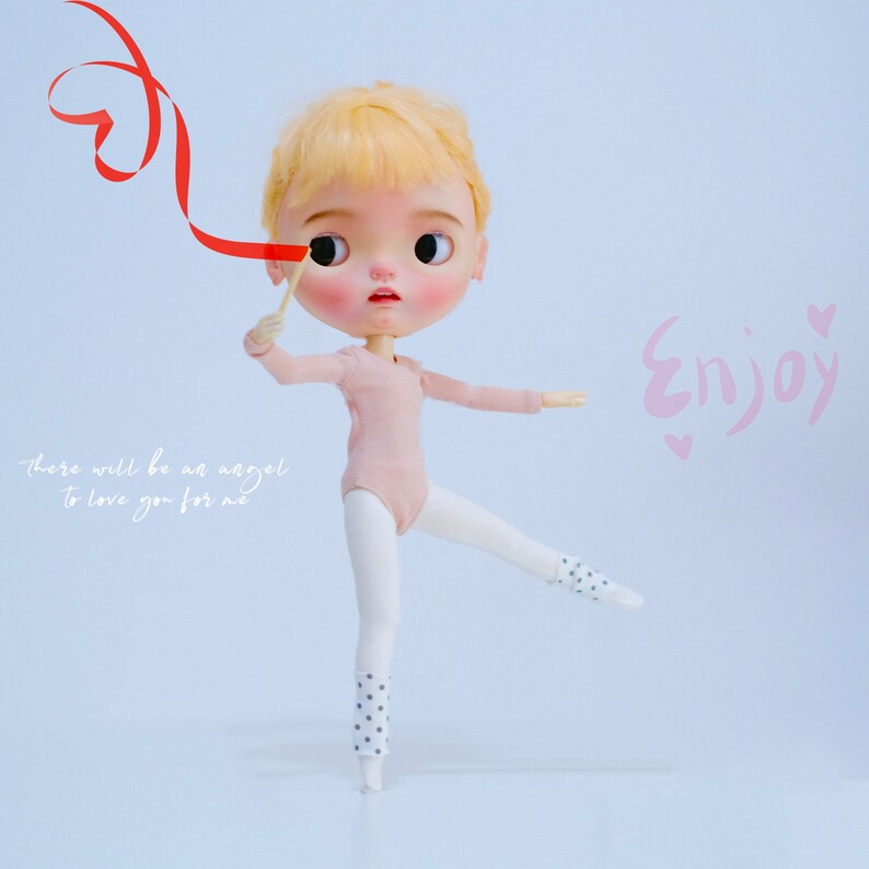 May include: A doll with blonde hair wearing a pink leotard and white tights with black polka dots is holding a red ribbon in the shape of a heart. The doll is standing on one leg with the other leg extended out to the side. The background is a light blue. The text "Enjoy" is written in pink on the right side of the image. The text "there will be an angel to love you for me" is written in white on the left side of the image.