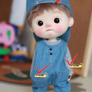 May include: A blue denim doll outfit with a striped shirt underneath, a blue denim cap, and grey sneakers. The doll has brown hair and large eyes.