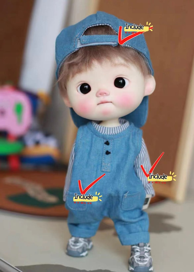 May include: A blue denim doll outfit with a striped shirt underneath, a blue denim cap, and grey sneakers. The doll has brown hair and large eyes.