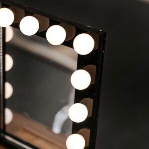May include: A black vanity mirror with a rectangular frame and a row of white light bulbs around the perimeter.