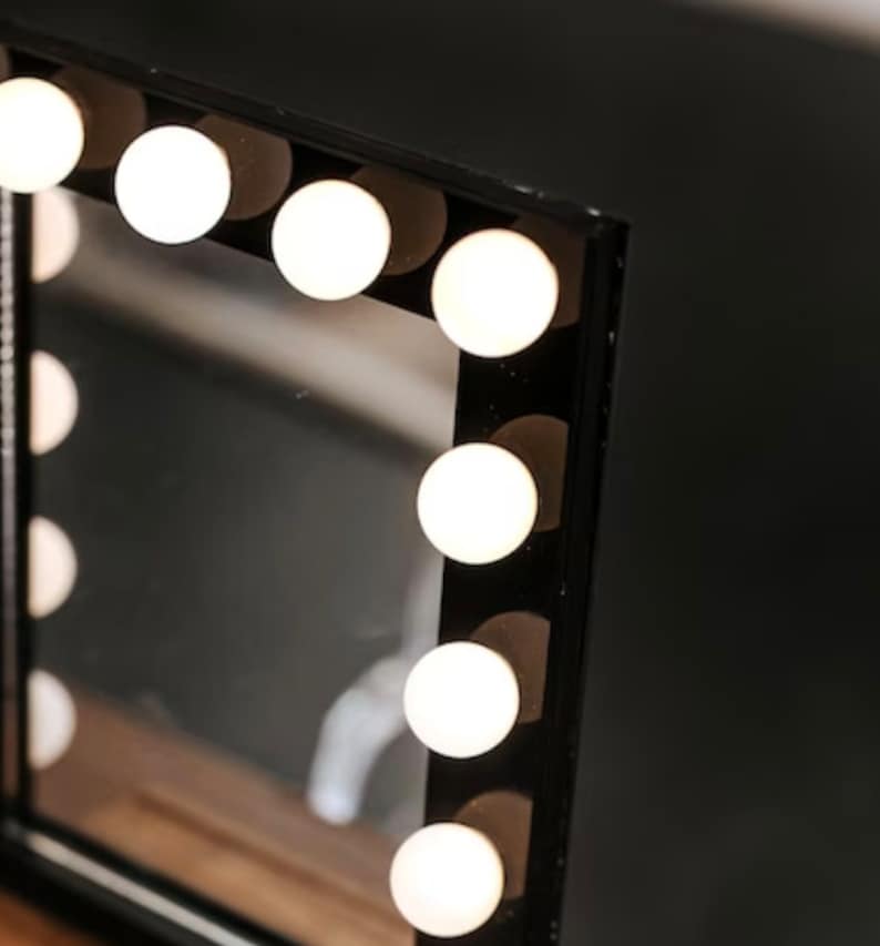 May include: A black vanity mirror with a rectangular frame and a row of white light bulbs around the perimeter.