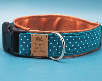 May include: Teal blue dog collar with white polka dots and a brown leather backing. The collar has a black buckle and a silver D-ring. A brown rectangular tag with the text "Noah Meets Scottie" is attached to the collar.