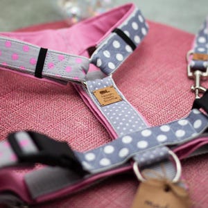 May include: A pet harness and matching leash set featuring a grey fabric with white polka dots and a pink fabric with grey polka dots. The harness includes black plastic buckles, metal D-rings, and a tan leather tag labeled Noah Meets Scottie.