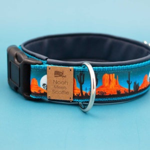 May include: A blue dog collar with a desert sunset design and a brown tag that reads "Noah Meets Scottie".