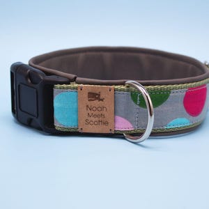 Könnte beinhalten: Ein graues Hundehalsband mit braunem Lederuntergrund und einem grün-weißen Polka-Dot-Muster. Das Halsband hat eine silberne Schnalle und einen silbernen D-Ring. Das Halsband hat ein braunes Leder-Etikett mit der Aufschrift "Noah Meets Scottie" und einer kleinen Walgrafik.