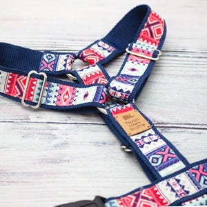 Könnte beinhalten: Ein marineblaues Hundegeschirr mit einem farbenfrohen geometrischen Muster in Rot, Rosa, Weiß und Blau. Das Geschirr hat silberfarbene Metallbeschläge und ein kleines Lederetikett mit Text. Das Design ist im Tribal- oder Südweststil gehalten.