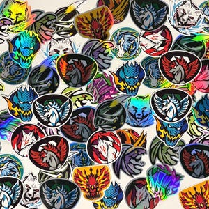 Op de afbeelding: Een verzameling van talloze ronde en schildvormige stickers met holografische afwerkingen. De ontwerpen bevatten diverse mythische wezens, gevleugelde paarden, draken, wolven en gepantserde helmen in levendige kleuren zoals rood, blauw en groen.