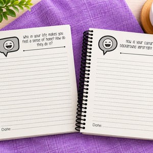 Puede incluir: Dos cuadernos de espiral con papel blanco rayado. La p&aacute;gina izquierda presenta un icono de burbuja de di&aacute;logo con una cara sonriente y el texto: Who in your life makes you feel a sense of home? How do they do it? La p&aacute;gina derecha tiene el mismo icono y el texto: How is your culture or background important to you? Ambas p&aacute;ginas incluyen una l&iacute;nea de fecha en la parte inferior.