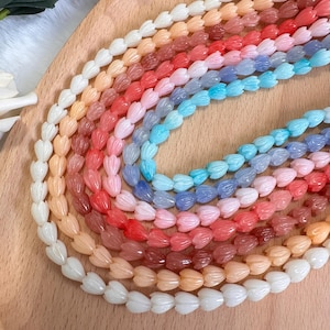 May include: A collection of beaded necklaces in a variety of colors, including white, peach, red, pink, blue, and purple. The beads are shaped like flower petals and are arranged in a rainbow pattern on a wooden surface.