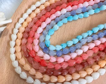 May include: A collection of beaded necklaces in a variety of colors, including white, peach, red, pink, blue, and purple. The beads are shaped like flower petals and are arranged in a rainbow pattern on a wooden surface.