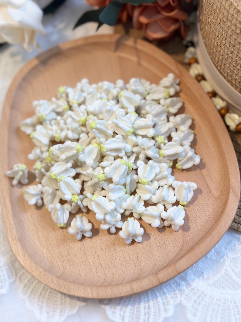 May include: A wooden tray filled with small, white, flower-shaped decorations with yellow centers. The decorations are clustered together, creating a textured surface. The tray is made of light-colored wood.