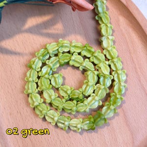 May include: A necklace made of light green flower-shaped beads. The beads are arranged in a circular pattern. The text "02 green" is in the lower left corner. The text below reads "Not all crown flowers beads are solid-colored - some come with beautiful gradient shades oh~!"