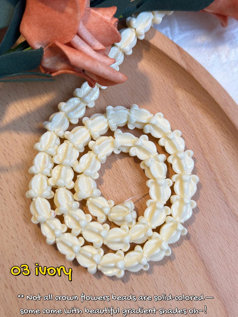 May include: Ivory-colored necklace composed of flower-shaped beads. The beads are arranged in a circular pattern on a wooden tray, with a peach-colored flower in the background. Text on the image reads "03 ivory".