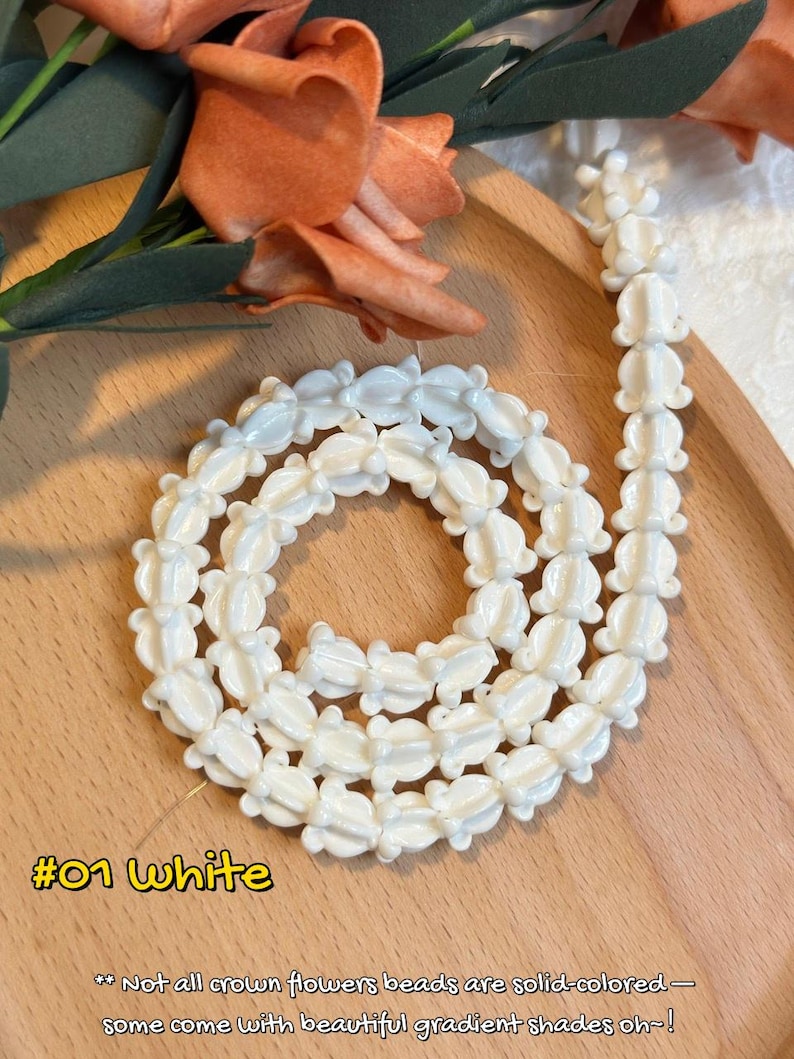 May include: White flower-shaped beads strung together, forming a necklace or strand. The beads are arranged in a spiral on a wooden surface. The image includes text that reads "#01 White" and a description about the beads.