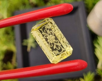 May include: A yellow, rectangular, carved gemstone with a floral design. The gemstone is held by red chopsticks.