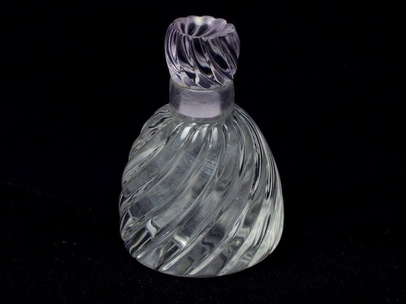 May include: A clear glass bottle with a swirling, textured design. The bottle has a purple glass stopper with a similar swirling design.