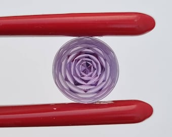 Puede incluir: Un cabujón de vidrio morado con un diseño geométrico. El cabujón está sujeto por un par de pinzas rojas.