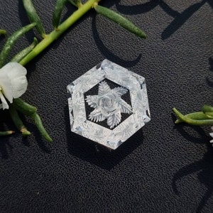 May include: A white hexagonal-shaped decorative object with a carved floral design. The design features a central rose with surrounding leaves.