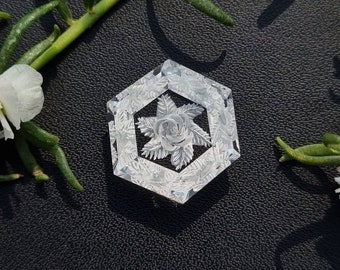 May include: A white hexagonal-shaped decorative object with a carved floral design. The design features a central rose with surrounding leaves.