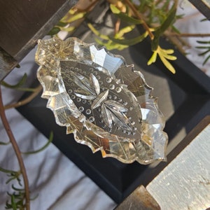 Könnte beinhalten: Ein klarer Glasanhänger mit einem ausgeschnittenen Design aus Blättern und Punkten. Das Glas hat einen goldenen Farbton und ist leicht schillernd.