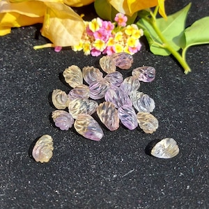 May include: A collection of small, translucent, teardrop-shaped beads in shades of lavender, peach, and clear. The beads have a textured, ridged surface. The image is set against a dark background with yellow and pink flowers.