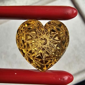 May include: A heart-shaped, faceted, golden-yellow gemstone with a starburst pattern.