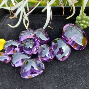 May include: A collection of eight purple amethyst gemstone chips, each with a unique shape and size, displayed on a black velvet surface.