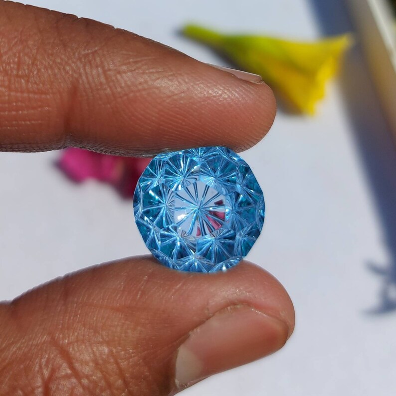 May include: A faceted blue topaz gemstone with a starburst pattern. The gemstone is round and has a high polish.