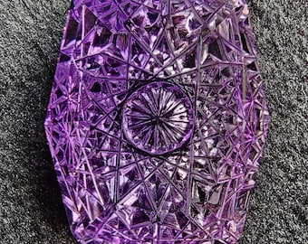 Puede incluir: Una piedra preciosa de amatista púrpura con un diseño facetado en forma de estrella. La piedra preciosa está tallada en una forma única y tiene un alto nivel de detalle.