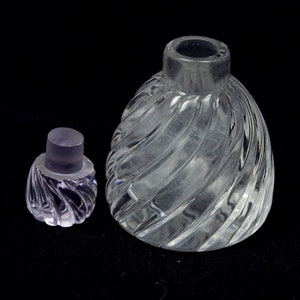 May include: A clear glass bottle with a swirling design and a matching stopper. The bottle is empty and has a round shape.